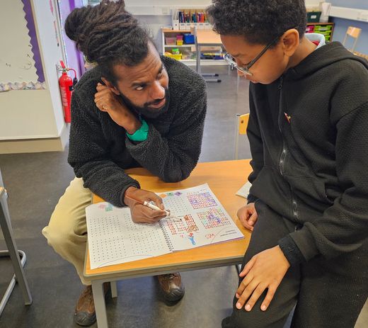 A mentor explaining an activity to his mentee. Both are wearing black hoodies and are facing each other. 