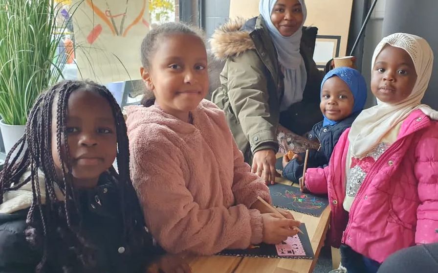 A group of children in colourful clothes and an adult sitting around a table and looking at the camera.
